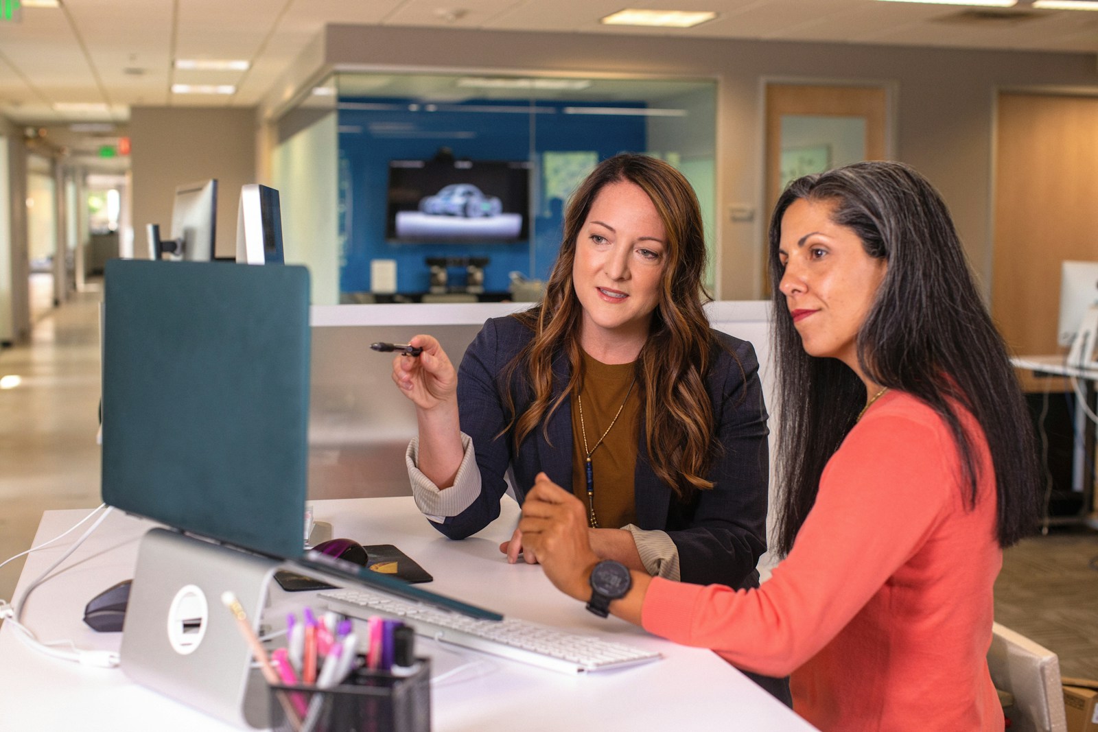 Twee vrouwen in gesprek aan een bureau met laptop